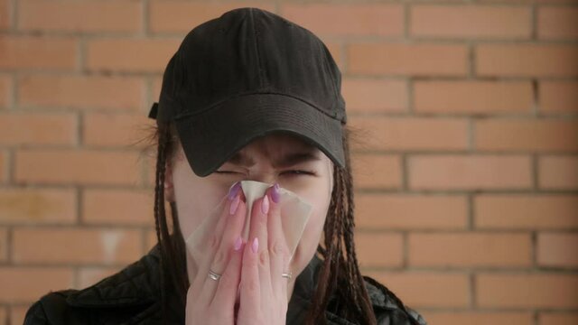 Young caucasian girl in black cap sneezes and blows her nose.