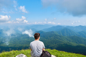 Fototapeta na wymiar A man smokes a VAPE on a mountain. A man enjoys a beautiful view of a green valley and smokes an electronic cigarette