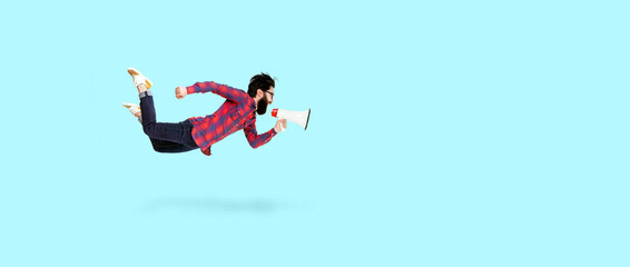 Bearded hipster man in glasses, jumping and shouting in megaphone, photo over blue background