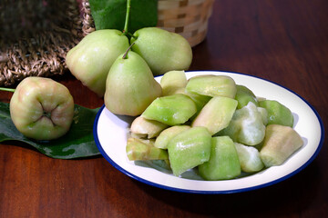 Rose apples and cut sliced piece in white dish on dark wooden table