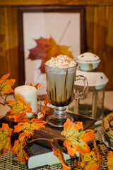 
Hot mocha in an irish glass, with a lantern and candles on the table, surrounded by autumn leaves in warm colors with a blurred background.