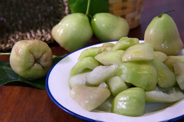 Rose apples and cut sliced piece in white dish on dark wooden table