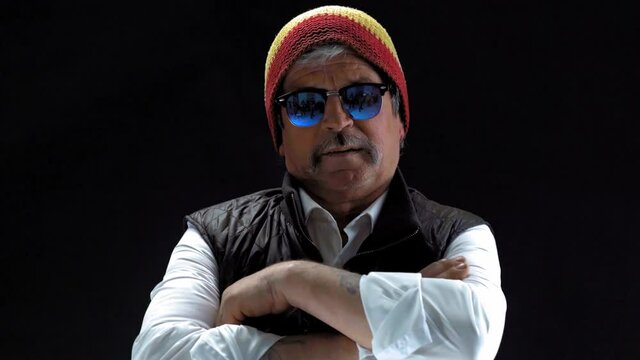 Hipster old man in a rastaman hat and sunglasses putting hands together on a chest and nod head in a dark room isolated on a black background. Prores 422.