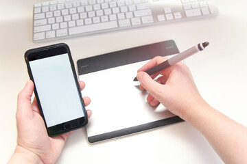 Minimalist Workstation with Hands Holding a Pen Tablet and a Smartphone.