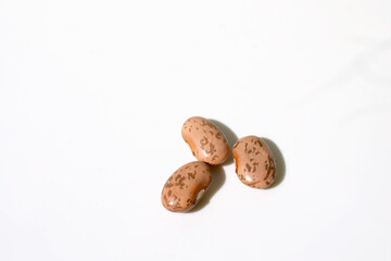 Three uncooked pinto beans on a white background with strong shadows. 