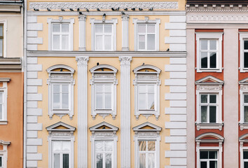 Fototapeta premium Beautiful decorative architecture in Lviv, Ukraine. Windows on the yellow and white facade of the house in the central historical part of the city. Pigeons are sitting on the ledge.