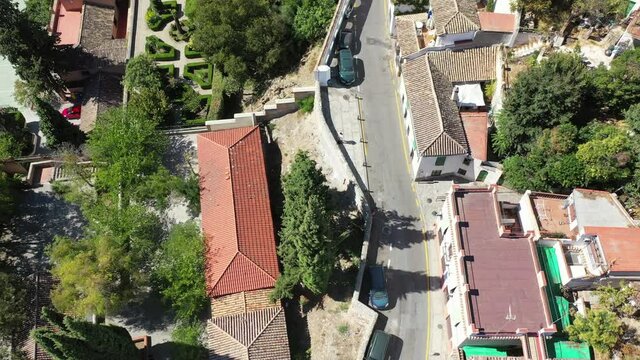 Aerial shot of street by houses and trees in city on sunny day, drone flying backward over residential buildings - Granada, Spain