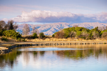 Sunset views of Shoreline Lake, with trees reflected in the calm water surface; Diablo Mountain Range visible in the background; Mountain View, South San Francisco Bay Area, California
