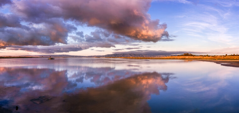 Sunset views of the restored wetlands of South San Francisco Bay Area, with dark clouds reflected on the water surface and Diablo Mountain Range visible in the background, Mountain View, California