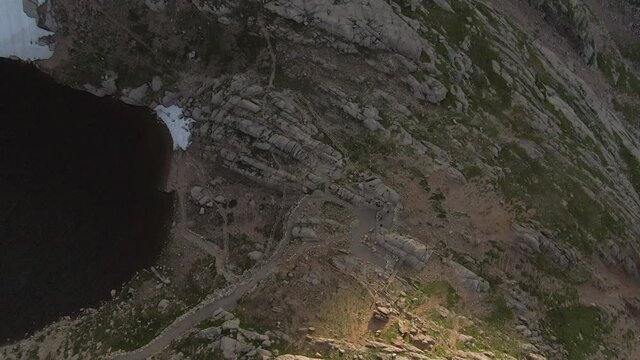 Aerial tilt up shot of people hiking on rocky mountain by lake, drone flying forward towards peak against sky - Mount Evans, Colorado