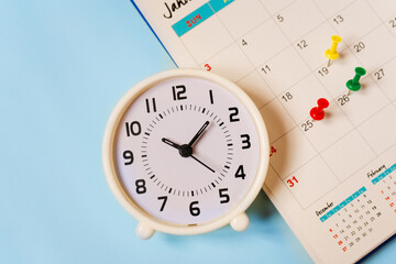 white analog clock with pin marked on calendar on blue paper background