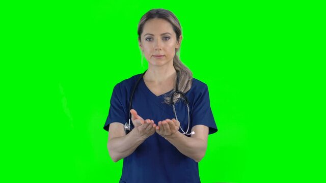 4K female nurse doctor on green screen isolated with chroma key. Woman holding empty space with both hands, offering invisible object in palms. Copy space for text or image. Front view
