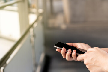 Young Asian woman using a touch screen smartphone while walking at the crowded place. Woman addicted social network all of the day. Woman talk to her friend by using smartphone. Copyspace in photo.
