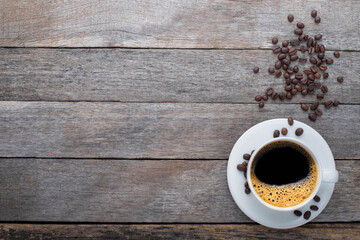 Top view, above from of Hot fresh black coffee with milk foam for morning menu in white ceramic cup with coffee beans roasted on rustic old wooden table background. Flat lay with copy space for text.