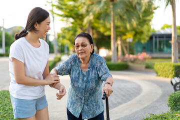 Granddaughter assist her grandmother whose age almost 90 years old exercise by walking at the park in the morning. Asian woman helping retired elder woman walking. Healthcare, wellness and wellbeing.