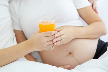 Lovely Asian family portrait, husband tenderly giving an orange juice to his pregnant wife. 