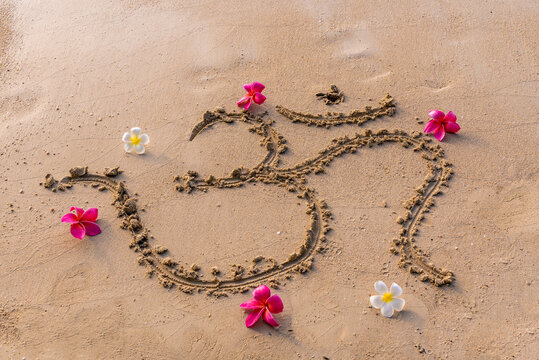 The sound "Om" or "AUM" written in Sanskrit - in the Hindu and Vedic traditions - sacred sound, the original mantra. Used in yoga practices and meditation techniques. Frangipani flowers on the sand
