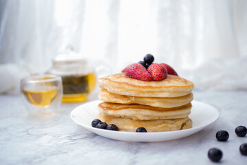 Stack of pancakes with topping, strawberry and blueberry.Placed in a white plate on a marble table and copy space.Eat with tea in the glass.