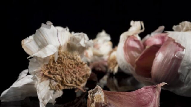 Moving macro view past garlic cloves and garlic bulbs on black glass and black background, amazing closeup footage