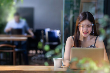 Pretty woman wearing face shield for healthcare, Young Asian woman sitting in coffee shop and working on laptop