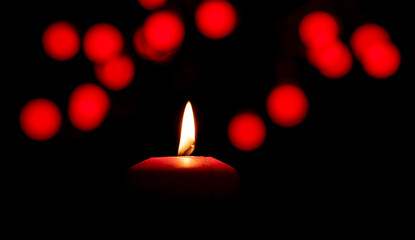 A red candle is burning. Red lights glow in the dark background. Festive lighting concept