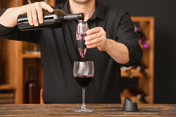 Man with bottle of wine, glass and aerator in cellar