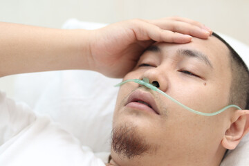 Asian male patient with nasal cannula staying in hospital room alone. Uncomfortable sick man look pensive lying in bed. Oxygen tube on his nose