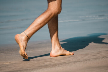Man's legs bare feet walking by the sandy beach. Copy space 