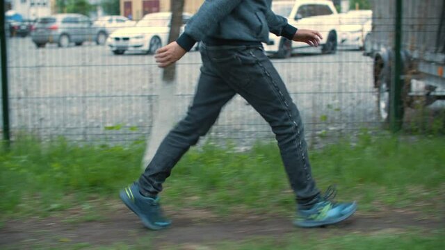 Running Teen Boy Street. Cropped Shot Of Unrecognizable Boy In Casual Clothing Running On Street. Side View Of Teenage Boy In Denim Pants And Sneakers Walking On Pathway In City