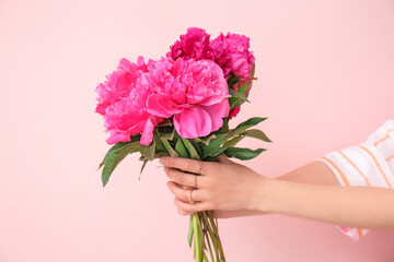 Female hands with beautiful peony flowers on color background