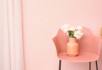 Vase with beautiful peony flowers on chair near color wall