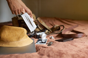      Travel idea with a hat and bag and a laptop with a hand picking a mask