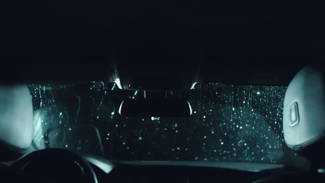 Drops flow down the windscreen. Inside view of a windshield car. Dark black cinematic picture. Process stage of polishing and washing a auto. Movement zoom camera dolly shooting platform.