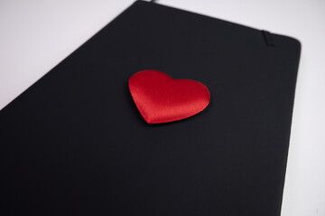 Red love heart on the black cover of a closed notebook or journal. Close up.