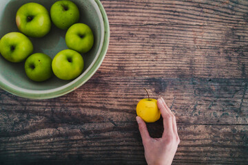 plant-based food, bowl of green apples and hand holding a smaller yellow one next to it