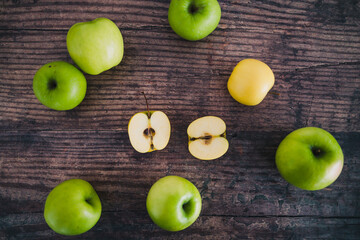 plant-based food, multitude of green and yellow apples scattered on wooden table with two halves in the centre