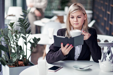 Young woman in cafe reading an ebook and drinking coffee