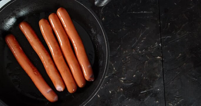 Sausages are fried in oil in a frying pan.