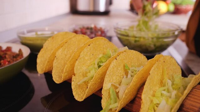 Woman hand making tacos, stuffing hard taco shells - adding the base layer of lettuce, camera orbit, close up. Phases of making tacos.