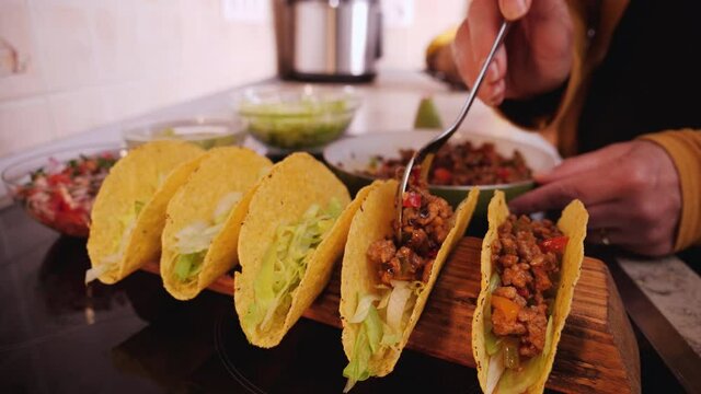 Woman hand stuffing hard taco shells - adding the ground meat and vegetables filling, camera orbit, close up. Phases of making tacos.