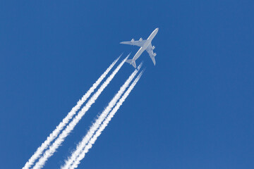 Large four engined commercial airliner jet aircraft flying at high altitude with a large contrail flowing behind it. - obrazy, fototapety, plakaty