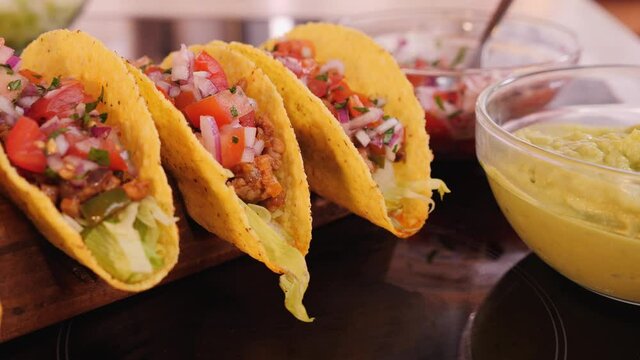 Hard taco shells in wooden holder with all the fillings added - waiting for the guacamole topping, camera orbit, close up - phases of making tacos
