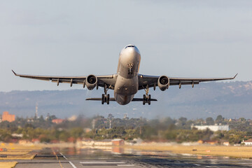 Large twin engine commercial airplane taking off from an international airport runway.