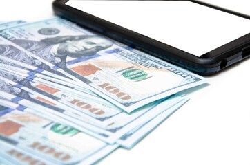 Dollars and smartphone. Banknotes in denominations of 100 dollars lie on a white background on them, next to them lies a smartphone with a white screen. Top view and angle Macro smartphone and dollars