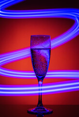 A glass of champagne on an orange background with the effect of drawing blue light on a long shutter speed. An idea for decorating a party or holiday with a neon effect