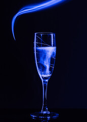 A glass of champagne on a black background with the effect of drawing blue light on a long shutter speed. Concept idea for decorating a party or holiday in neon style.