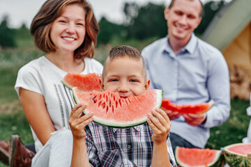 Happy family eating watermelon at picnic in meadow near the tent. Mother, father and child Enjoying Camping Holiday In Countryside