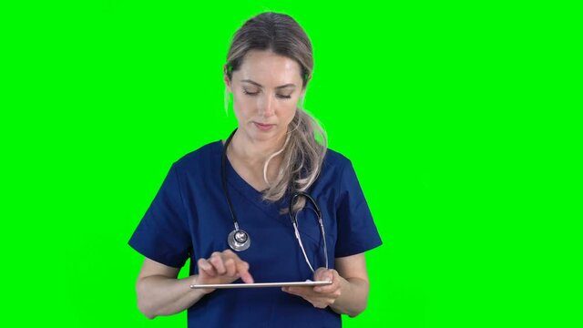 4K female nurse doctor on green screen isolated with chroma key. Woman holding digital tablet pressing buttons on virtual screen. Copy space for animation, text or image. Touchscreen gestures