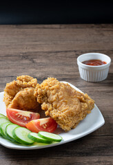 Crispy fried chicken served with slice tomato , sliced cucumber and ketchup on wooden background.