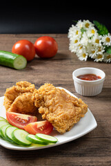 Crispy fried chicken served with slice tomato , sliced cucumber and ketchup on wooden background.